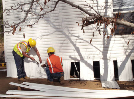 Picture of two workers installing skirting on a white mobile home.