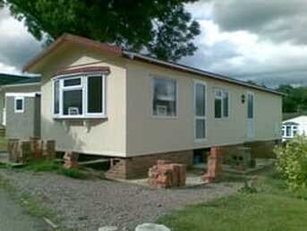 Picture of a tan colored mobile home with the brick skirting partially removed
