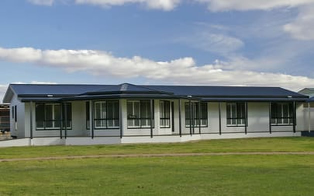 Picture of a gray mobile home with a dark blue roof with green grass on front of it.